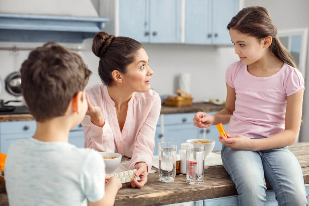 Caring mom. Smiling loving dark-haired young mother holding medications and talking with her kids about medication adherence