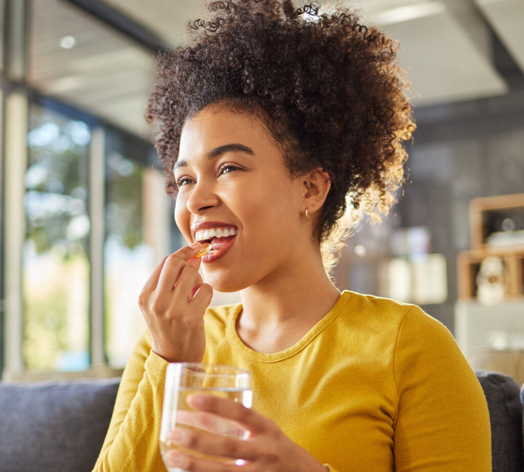 Glass, water and woman with medicine on sofa for health, self care and supplement at home. Relax, healthcare and happy african person with liquid drink and pill or tablet for Rx Adherence