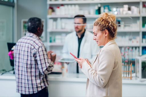 A pharmacist and an assistant engage with an elderly male customer in a pharmacy, discussing medications, highlighting personalized patient care