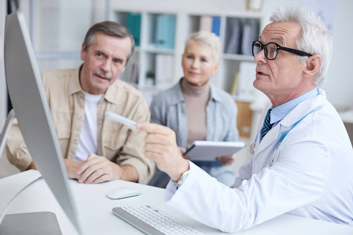 An elderly couple consults with a doctor who uses a computer to discuss health plans, demonstrating personalized healthcare consultations for senior patients.