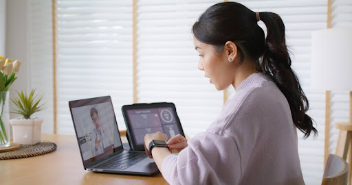 A female health professional conducts a remote consultation using multiple digital devices, exemplifying enhanced patient accessibility and care through telehealth