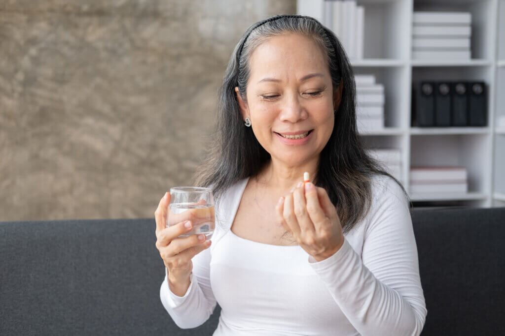 Happy elderly woman taking a pill to drive adherence according to the doctor order while sitting on the sofa.