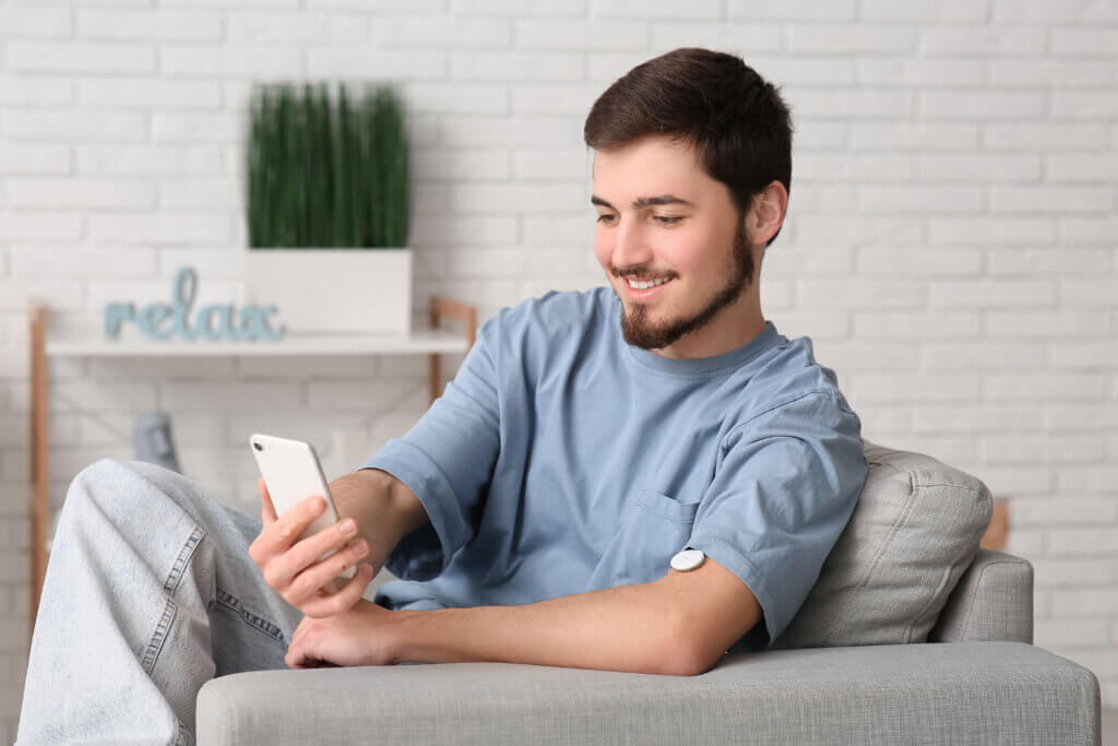 Diabetic young man with glucose sensor using mobile phone for measuring blood sugar level at home